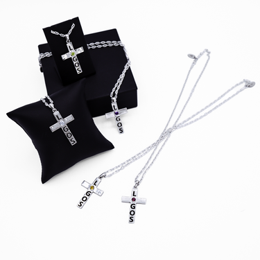 Sterling silver cross pendant with a chain, displayed on a black pillow and a black box, with gemstones set in the cross.